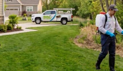 A pest control tech sprays a wooded area behind a home to treat for ticks